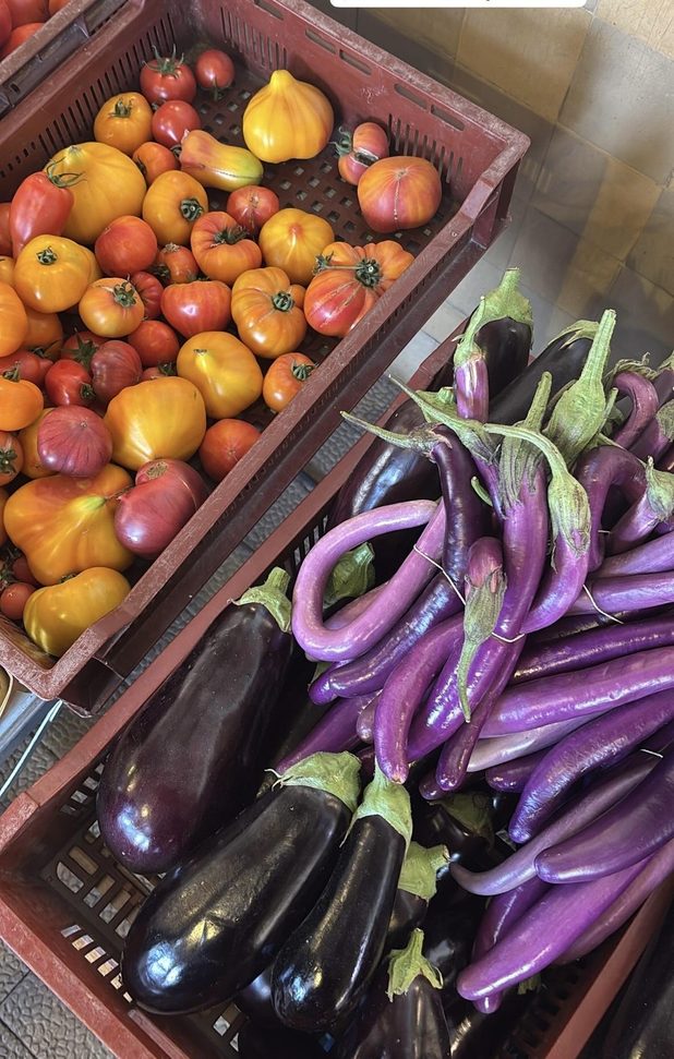 Heirloom tomatoes beside slender purple aubergines at a market stall